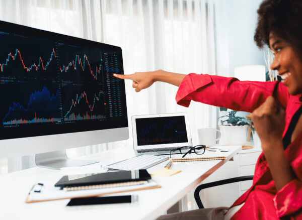 African woman blogger smiling on happy face, pointing on screen with valued stock market achievement at high profit. Concept of exchange investment online in trading application on pc. Tastemaker.