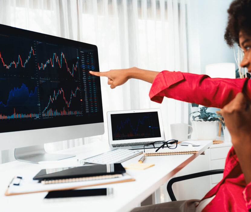 African woman smiling on happy face, point on stock market screen. Tastemaker. African woman blogger smiling on happy face, pointing on screen with valued stock market achievement at high profit. Concept of exchange investment online in trading application on pc. Tastemaker.